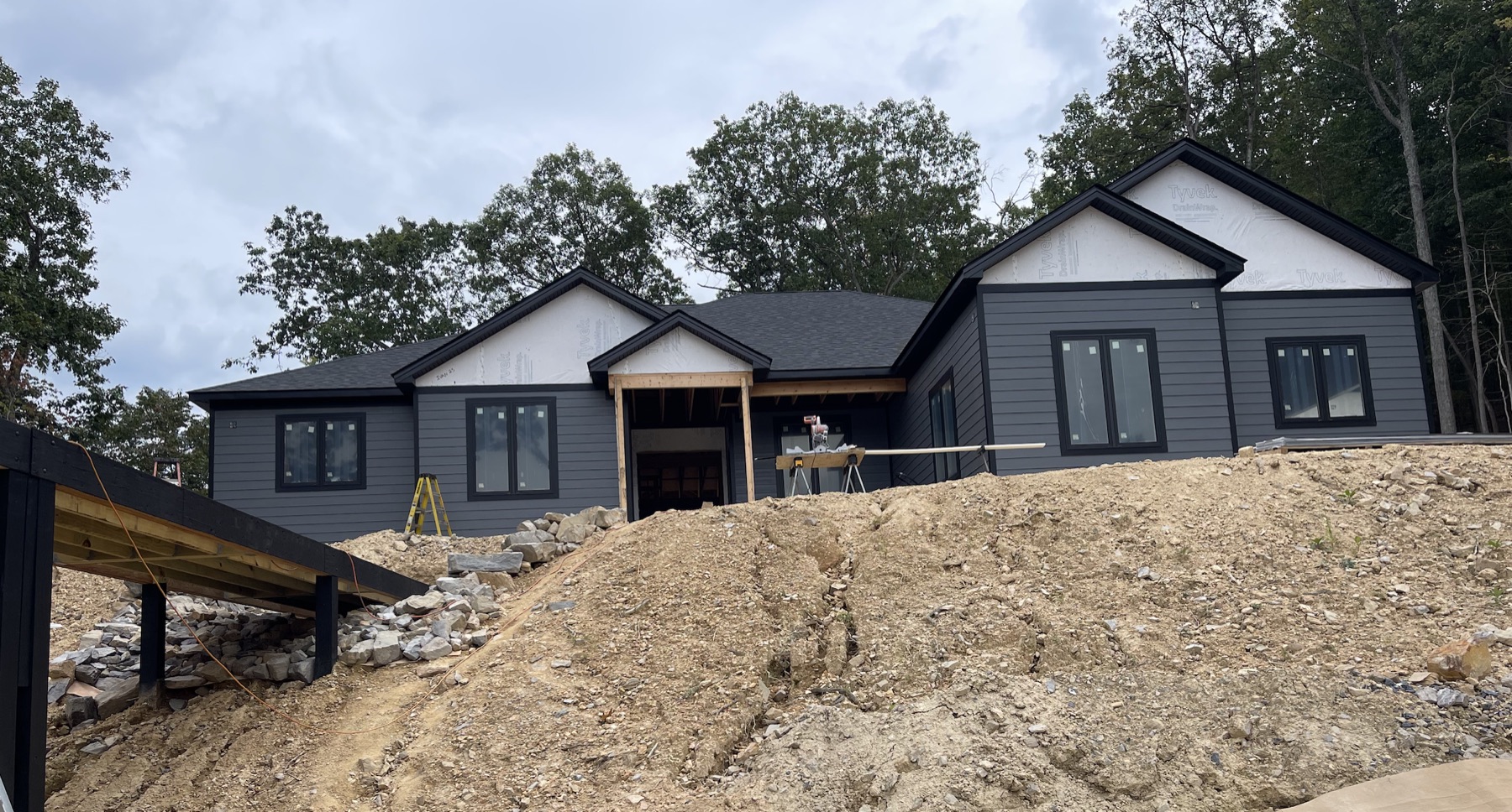 Expansive dark-gray custom home under construction on a wooded hillside